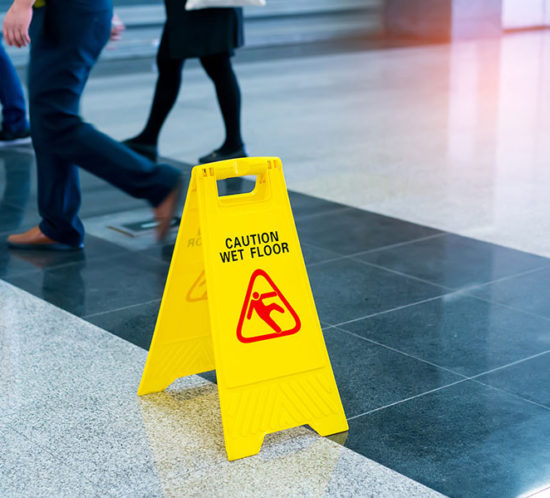 Photo of slippery floor with a caution sign and people walking near it