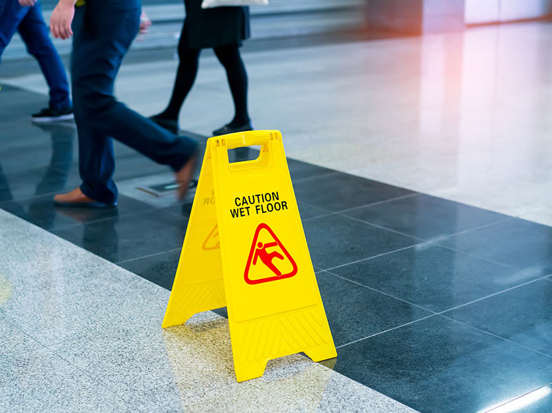 Photo of slippery floor with a caution sign and people walking near it