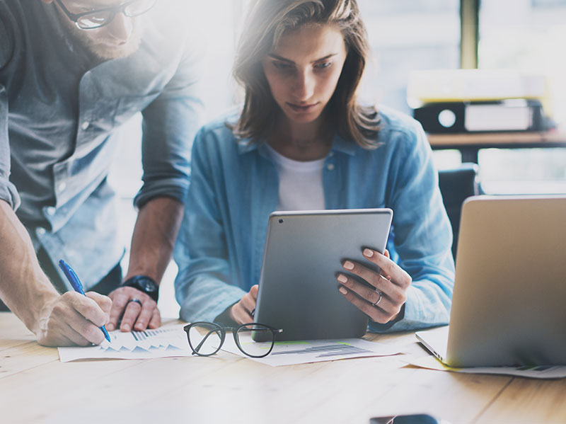 Man and woman looking at a website on a tablet and a laptop